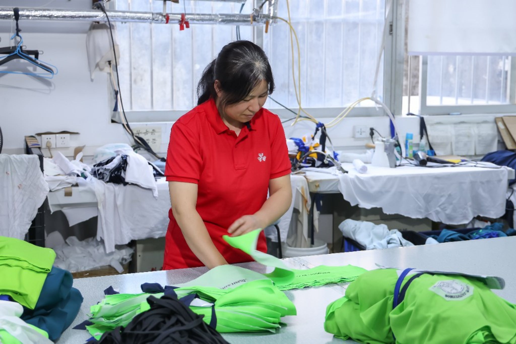 Factory workers inspecting finished custom team wear jerseys in apparel factory.