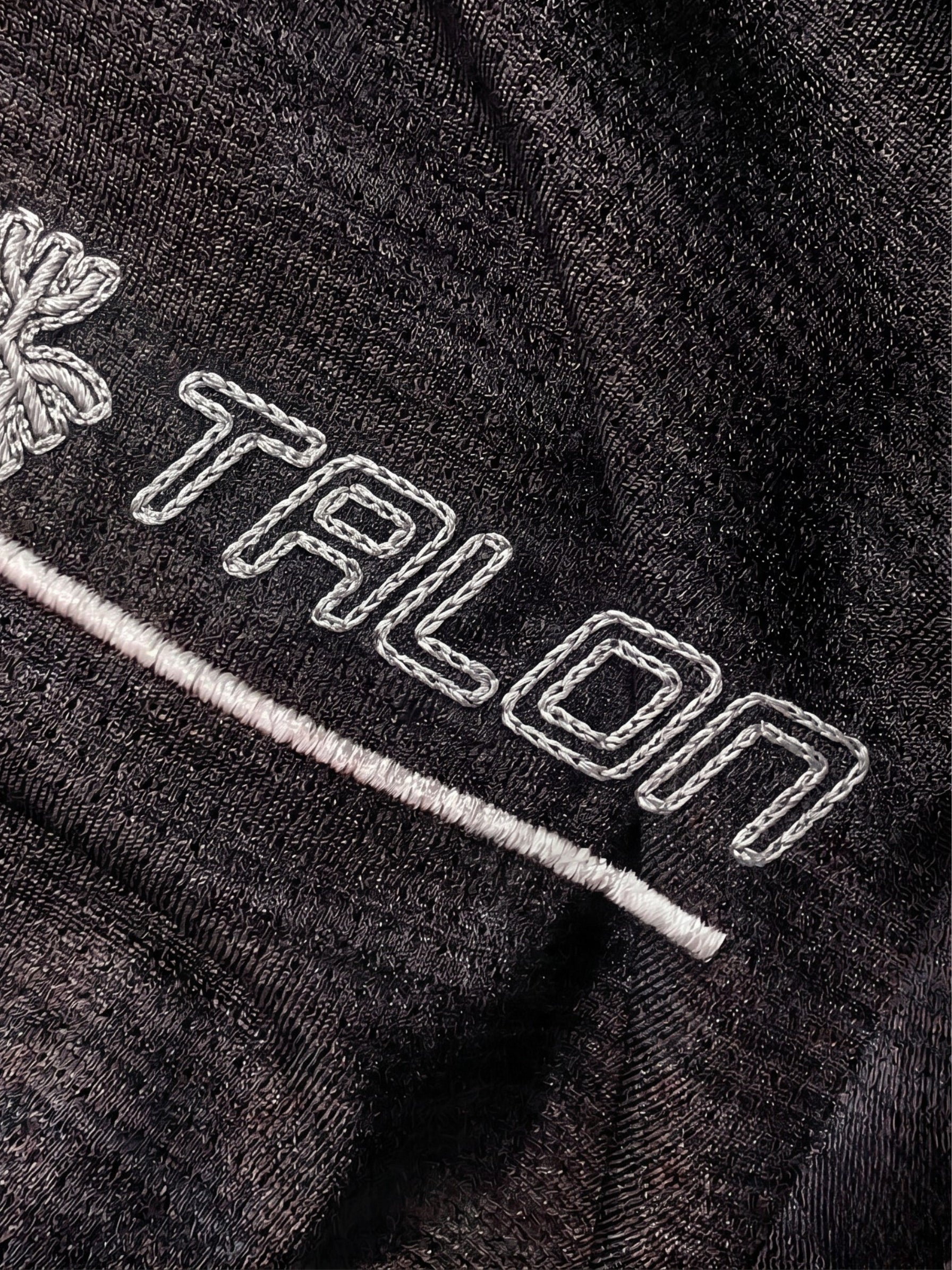 TALON chain stitch embroidery close-up on black technical mesh sportswear fabric.