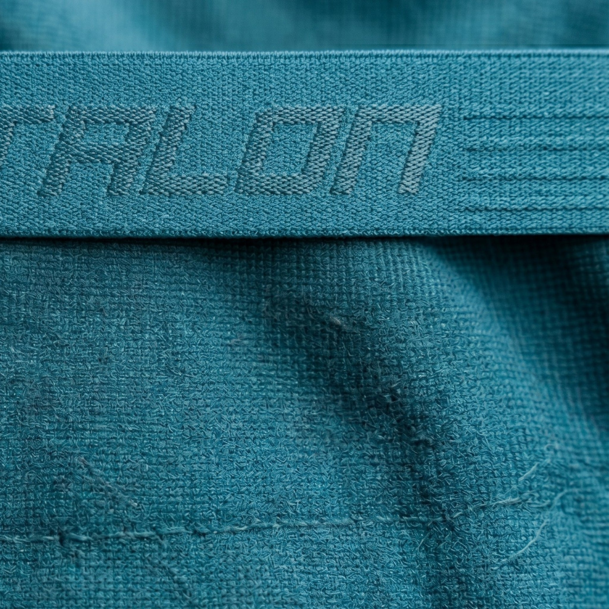 Tonal jacquard custom elastic waistband with woven branding on teal sportswear.