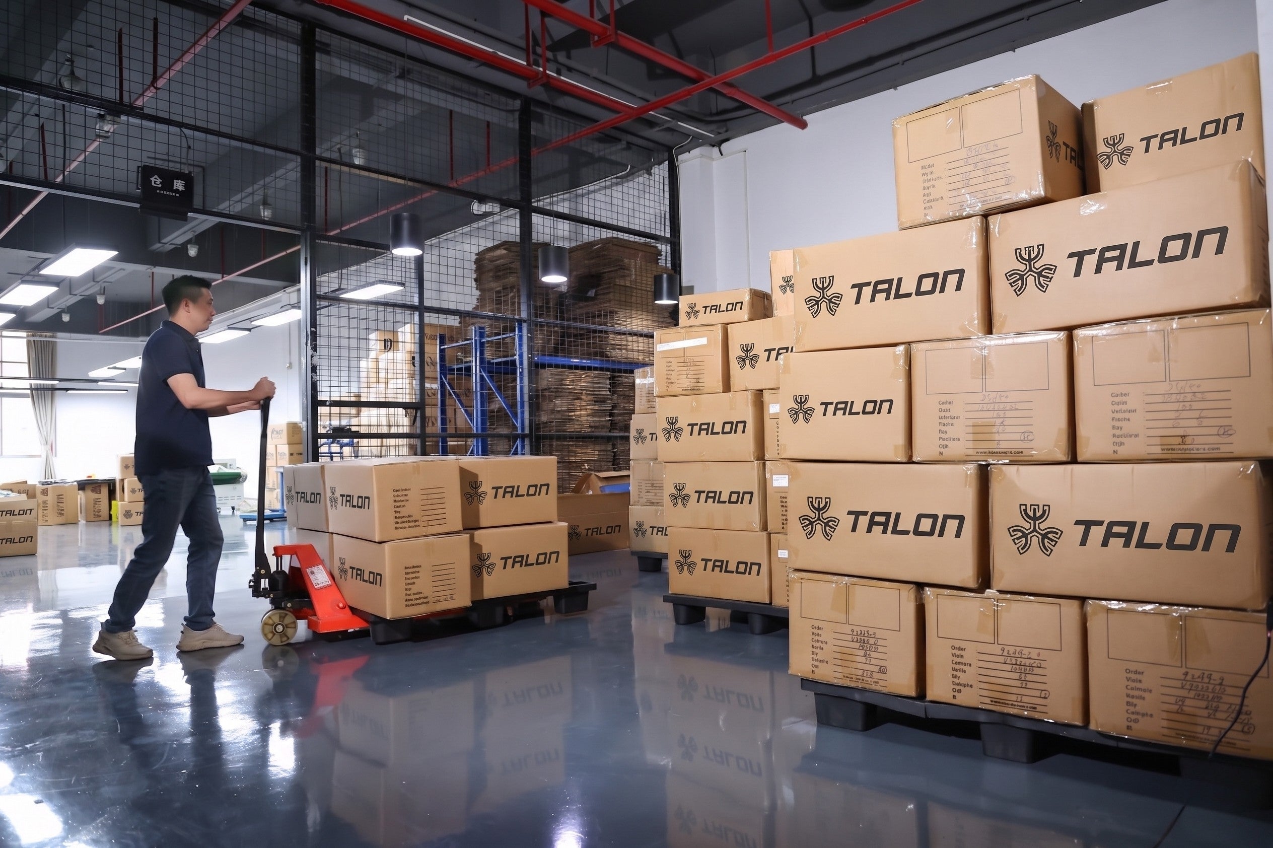 A man pushing a pallet jack with TALON boxes in a warehouse. — TALON OEM manufacturing